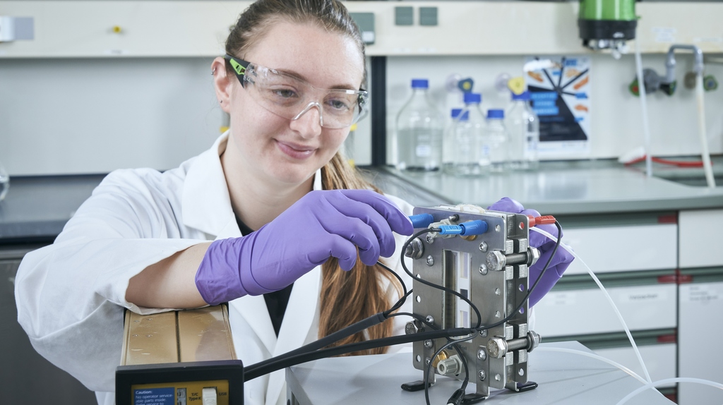 Frau mit Schutzbrille justiert eine Maschine